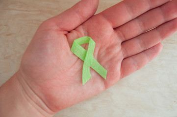 A hand holds a green awareness ribbon. World cerebral palsy day. World Kidney Day. International Day of Rare (Orphan) Diseases, World Mental Health Day