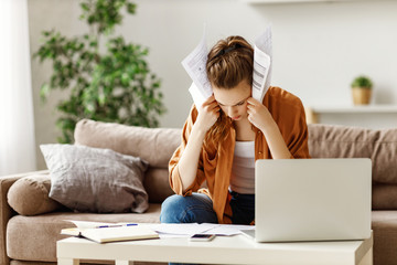 Pensive stressful female employee examining reports while working on complicated project at home.