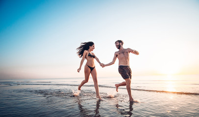 Romantic couple in love enjoy freedom running at the beach at sunset. Young people having fun at vacation outdoor.