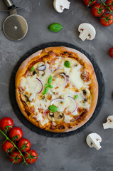 Homemade Italian vegetarian pizza with tomato sauce, mushrooms, cheese, onions and basil on a stone on a dark background. Vegetarian food. Vertical orientation. Top view.