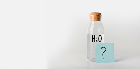 Glass bottle with the inscription chemical formula of water on it and question mark on a note sheet.