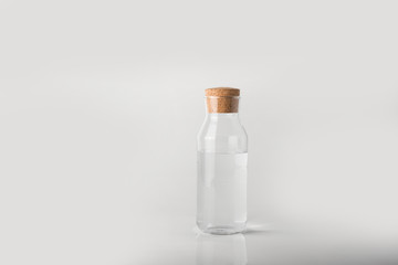 Image of a glass bottle on a white background with a cork stopper, inside which is clear transparent water.