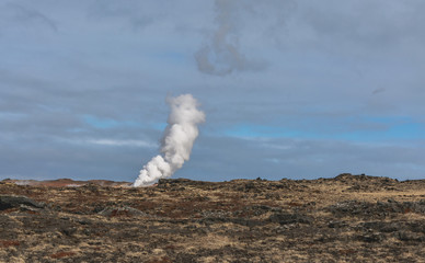 Geothermal area in Iceland.  Powerful steam jet above the ground. A smoking geyser on a background of yellow clay and a cloudy sky. Reykjanes Peninsula