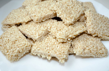 In a white round plate are square-shaped cookies of white sesame, honey and gluten-free sugar on a light table