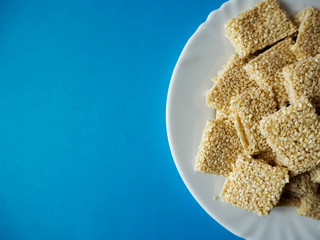 Part of a white steak plate with square shaped cookies of white sesame honey and sugar on a blue background. Gluten and egg free