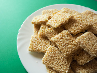 Part of a white steak plate with square shaped cookies of white sesame honey and sugar on a green background