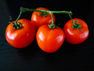 Four ripe red round tomatoes in one viscose on a black background