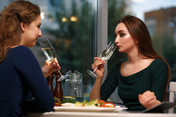 Two young successful women drink wine in a restaurant and celebrate the deal