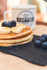 Delicious pancakes with blueberry, bananas and maple syrup on black dish