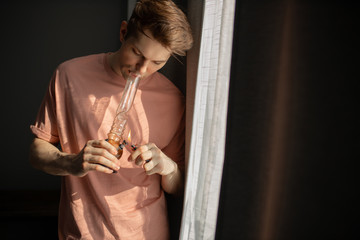 young man smokes bong cannabis weed at home. medical marijuana, hemp use and legalization of the...