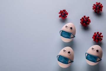 Eggs wearing medical mask for stop coronavirus and models of covid-19 virus on blue background. Epidemic coronavirus COVID-19 concept. Place fo text