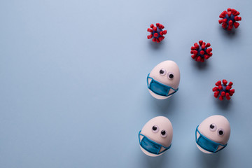 Eggs wearing medical mask for stop coronavirus and models of covid-19 virus on blue background. Epidemic coronavirus COVID-19 concept. Place fo text