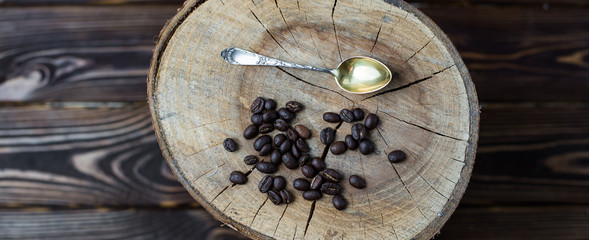 Fried coffee beans and a silver spoon on a wood background