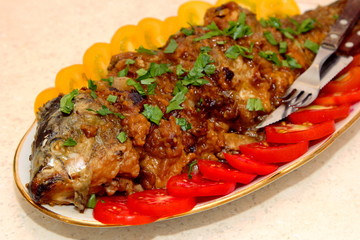 Fried carp with beer and cookies on a plate, decorated with red and yellow tomatoes, Old Czech fish recipe