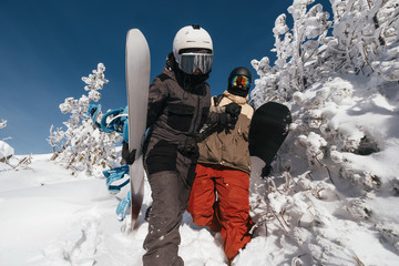 Fototapeta na wymiar Snowboarders holding boards walking by deep snow for freeride in winter mountains. Snow covered cliffs and trees