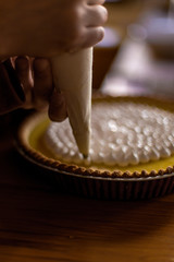 hands of a man using a piping/icing bag to frost a lemon pie