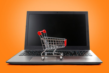 A laptop with a toy shopping cart sitting on the keyboard. Isolate on an orange background. Concept...