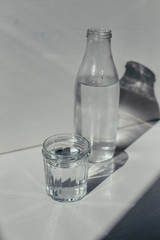 glass of water and glass bottle on a table in front of white backdrop