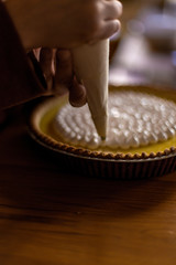 hands of a man using a piping/icing bag to frost a lemon pie