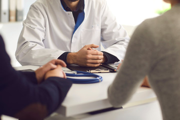 Confident doctor and couple patient sitting at the table in clinic office. Family doctor.
