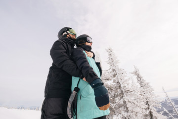 Fototapeta na wymiar Love couple of snowboarders outdoors in beautiful winter landscape with snow covered spruce trees