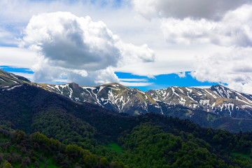 Naklejka na ściany i meble Beautiful mountain panorama with lush greens, blue skies, and puffy clouds