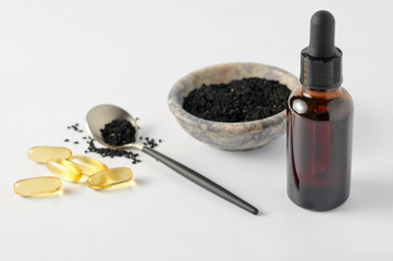 Glass bottle and pills of black cumin seeds essential oil. Nigella Sativa in spoon and bowl on white background