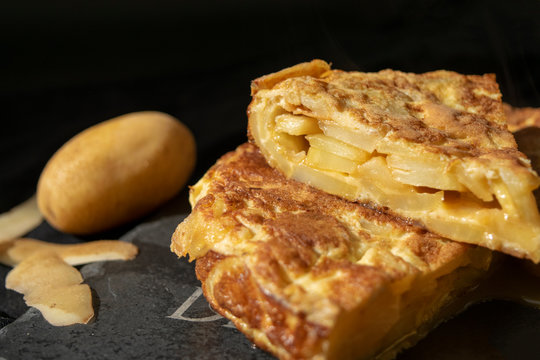 Spanish omelette photography with potato blurred behind and two pieces of tapas with black background