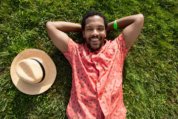 Black male, feeling happy to spend his free time very well laying on the green grass.