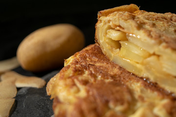 Spanish tortilla photography with potato blurred behind in a black background