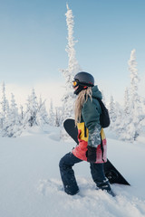 Female snowboarder wearing long dreadlocks and ratsa hoody in white winter forest walking in snow...