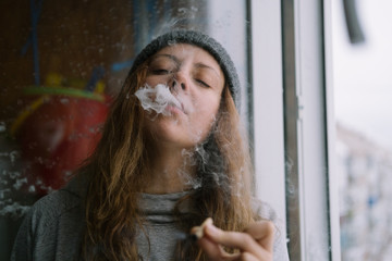Female wearing hat smoking self-roll weed cigarette blowing smoke