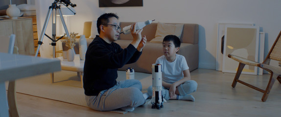 Chinese father and son playing together, building moon landing mission rocket together. Stay home, quarantine, science