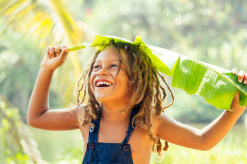 Mowgli indian boy with dreadlocks hair hiding holding banana leav as a rain cover in tropics green...