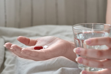 Close-up view of young woman's hands. Girl in bed holding tablets or pills and glass of water. Painkiller with space for text.