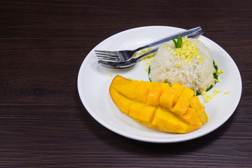 Sticky rice with fresh ripe mango with coconut milk put white plate on brown dark wooden table is thai style tropical dessert.
