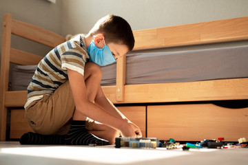 Stay at home quarantine coronavirus pandemic prevention. A boy in a protective medical mask plays and folds the constructor himself in his room. Prevention epidemic. COVID-19.