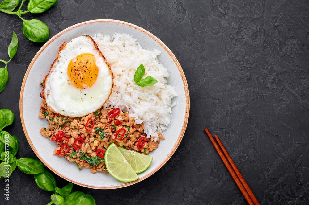 Wall mural pad krapow gai - thai basil chicken with rice and fried egg black slate background. pad krapow is th