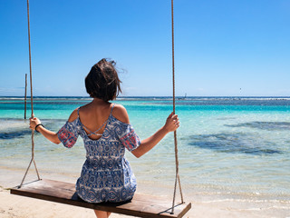 Young model on a swing at the Caribbean Sea looking to the horizon and it's turquoise waters.