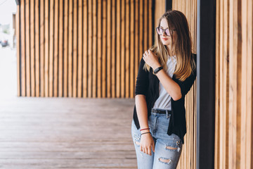 Fototapeta premium Portrait of a young woman on the wooden background with vertical boards. Beautiful girl with long hair and glasses smiling