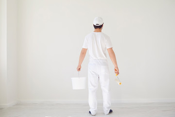 A male painter in a white uniform with a roller works in his hand in a white room