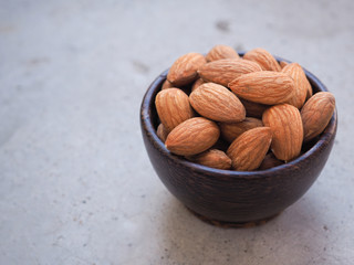 Organic almonds seeds in a wooden bowl put on a grey concrete background. Copy space for text..