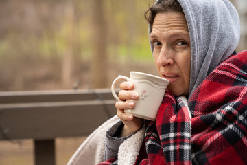 Middle age woman wrapped in a plaid wool blanket with coffee.