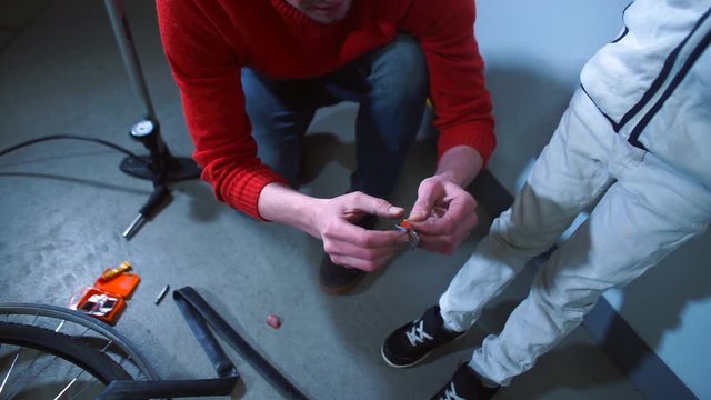 Father shows son rubber patch on the wheel. Sealing holes in the rubber of the wheel. Bike repair.
