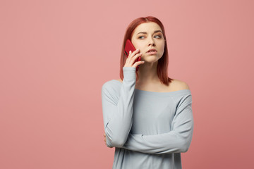 Serious woman talking on phone while standing in studio on pink background