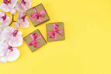flat-lay of Gift present boxes with pink ribbon on yellow background with orchid flower. spring concept. Copy space