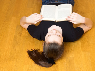 Young girl fell asleep reading a book on a brown wooden floor