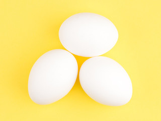 Three white chicken eggs on a yellow background. Healthy eating concept