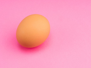 One brown chicken egg on a pink background with copy space. Healthy eating concept