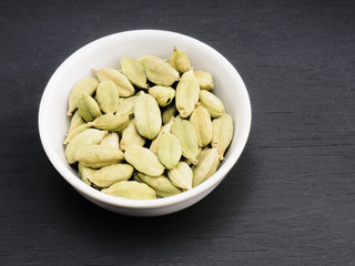 Spice green cardamom in white ceramic bowl on black wooden background. Healthy eating and organic food concept